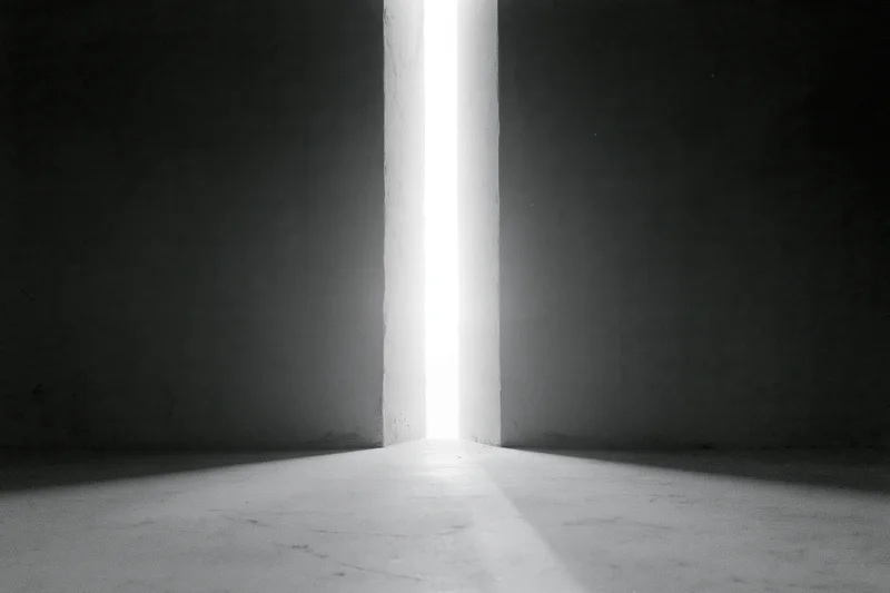 Narrow vertical gap between dark concrete walls letting in bright light onto floor