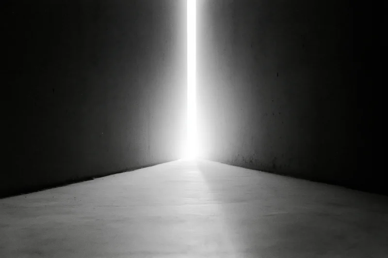Bright vertical light beam in narrow gap between dark concrete walls in a corridor