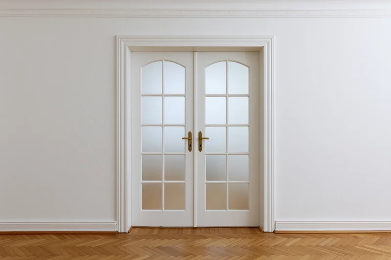 White double doors with arched frosted glass panels in a minimalist interior hallway