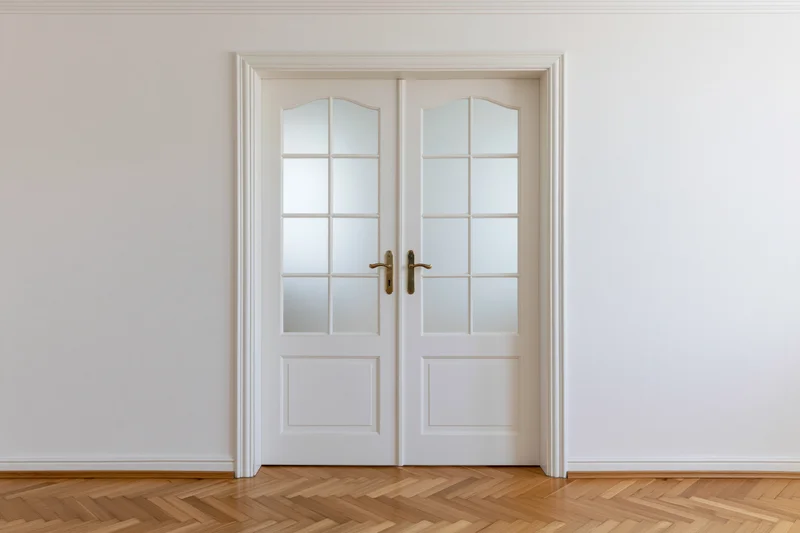 White double doors with arched frosted glass panels in a minimalist interior with parquet flooring