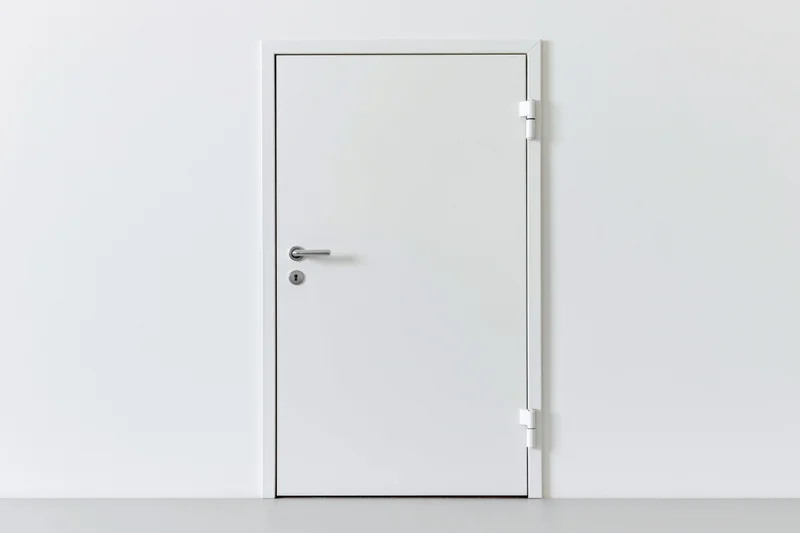 White steel door with lever handle and keyhole in a minimalist interior
