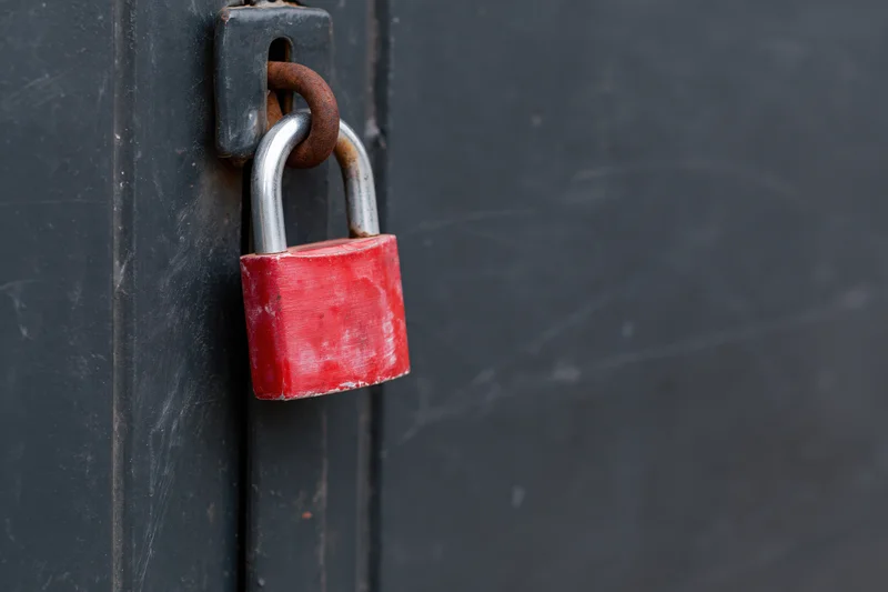 Red padlock secured on a rusted metal latch of a dark door