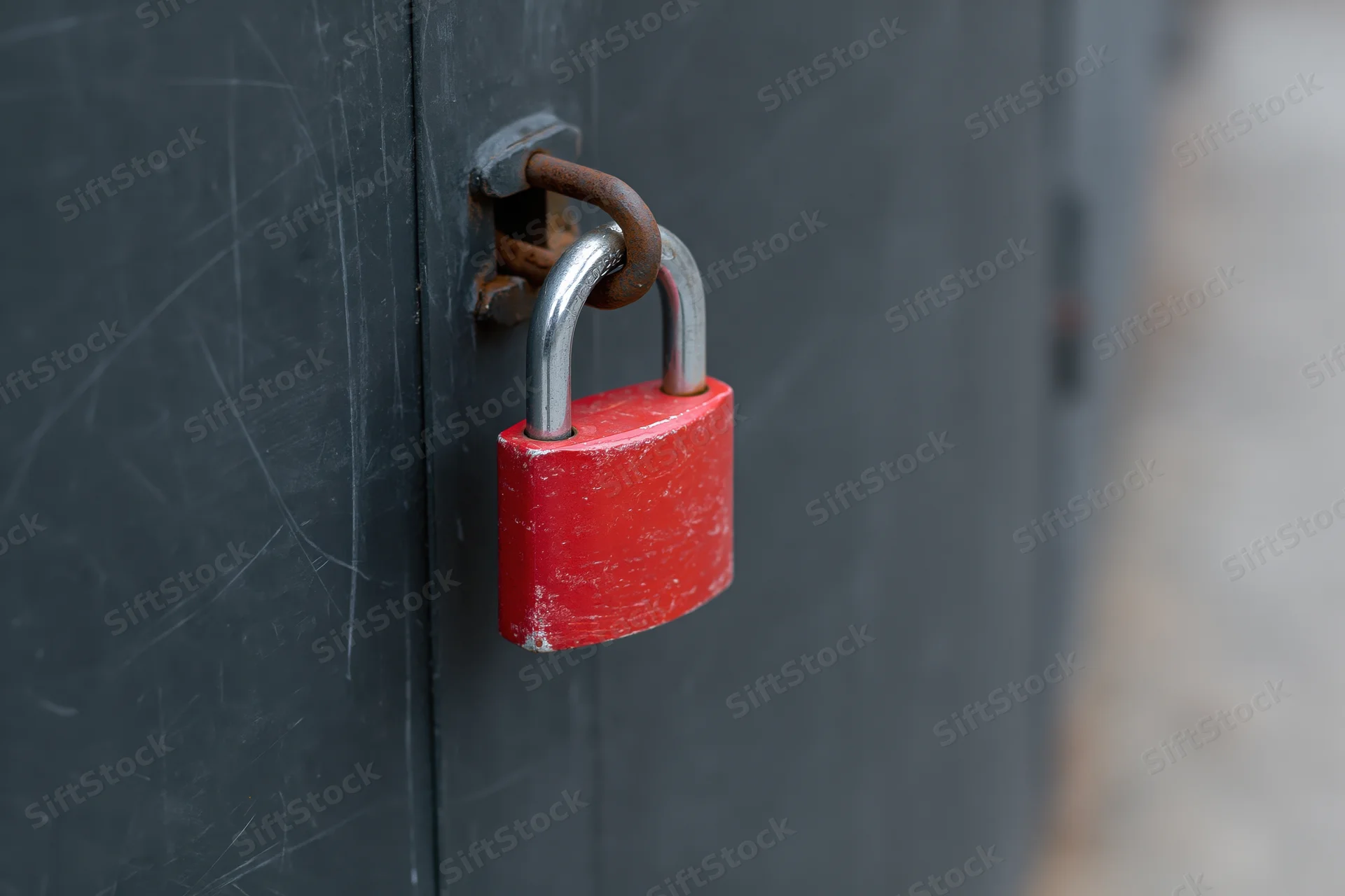 Red padlock secured on a rusted metal latch of a gray industrial door