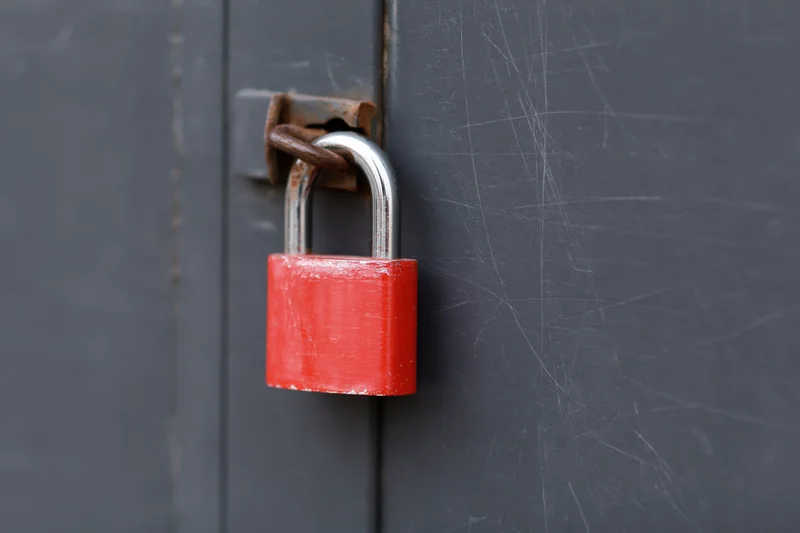 Red padlock secured on a rusted metal latch of a gray industrial door