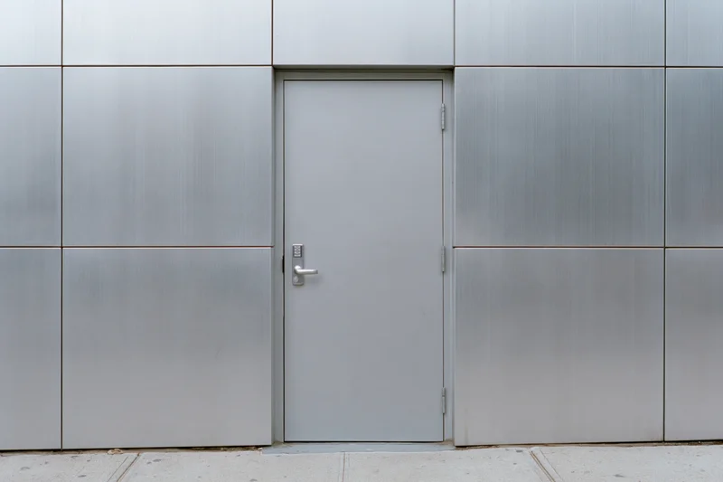 Gray metal utility door set into a flat aluminum panel facade