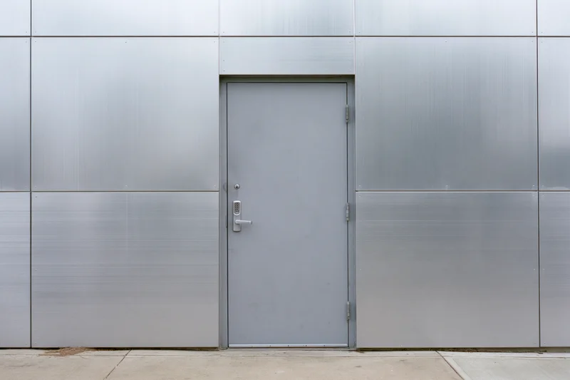 Gray metal utility door set into a flat aluminum panel facade