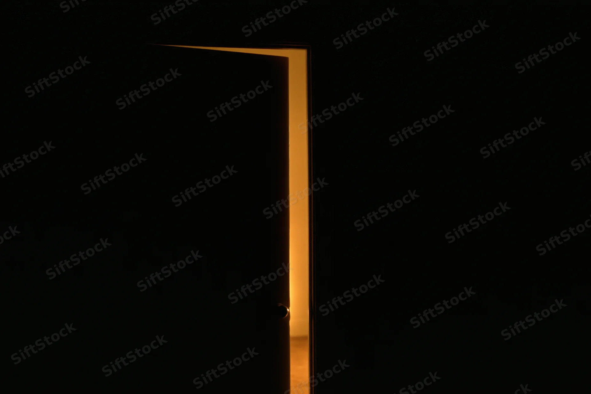 Slightly ajar interior door silhouetted against darkness with warm light glowing from the opening