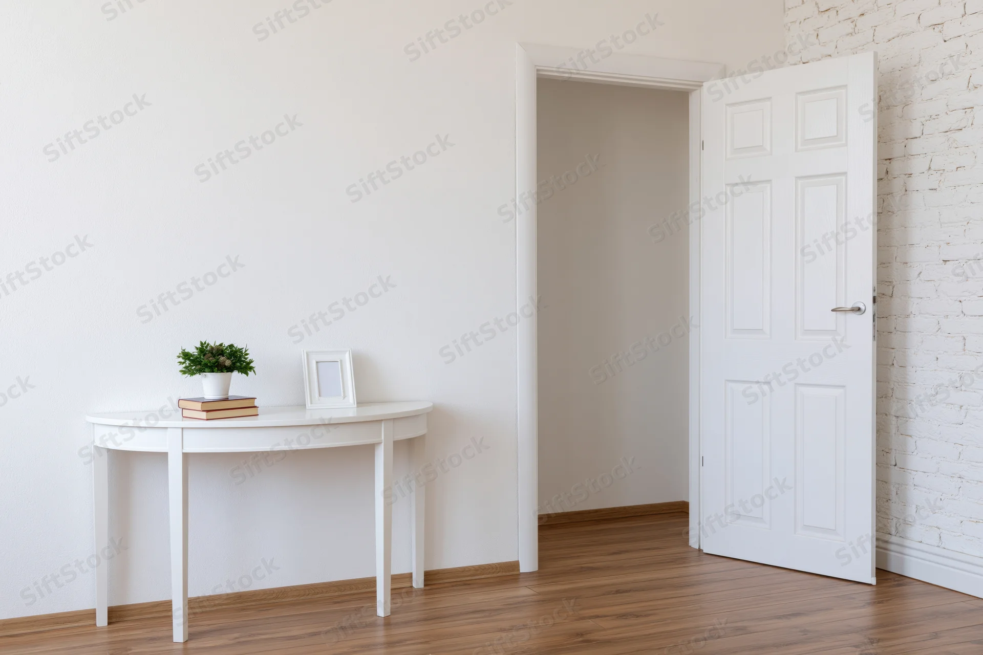 White console table with potted plant and picture frame in minimalist entryway with open door and wooden floor