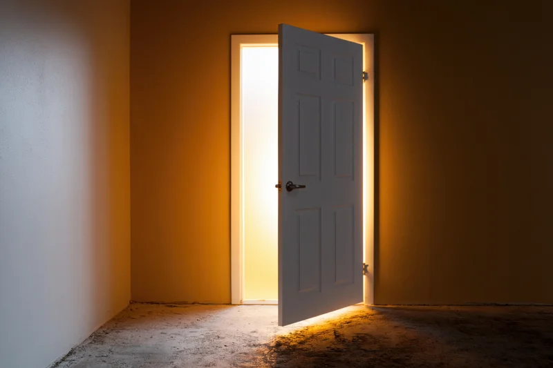 White interior door slightly ajar in an empty room with light streaming through