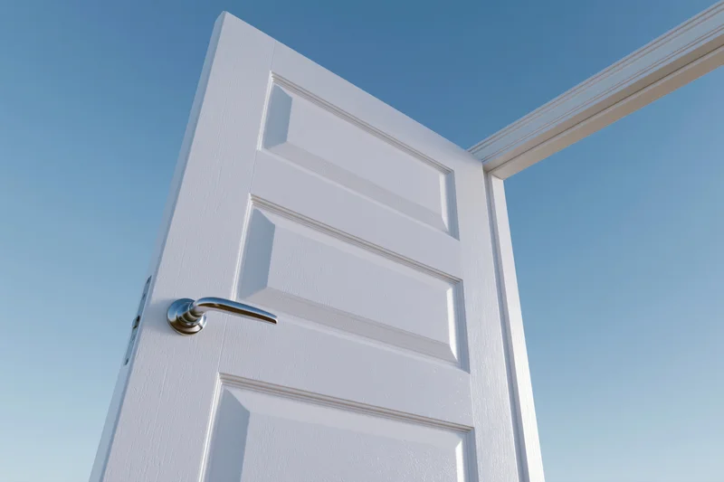 White paneled door with silver lever handle swinging open against blue sky