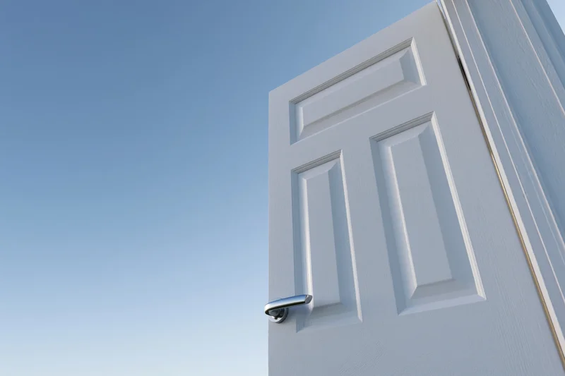 White paneled door with silver lever handle swinging open against blue sky