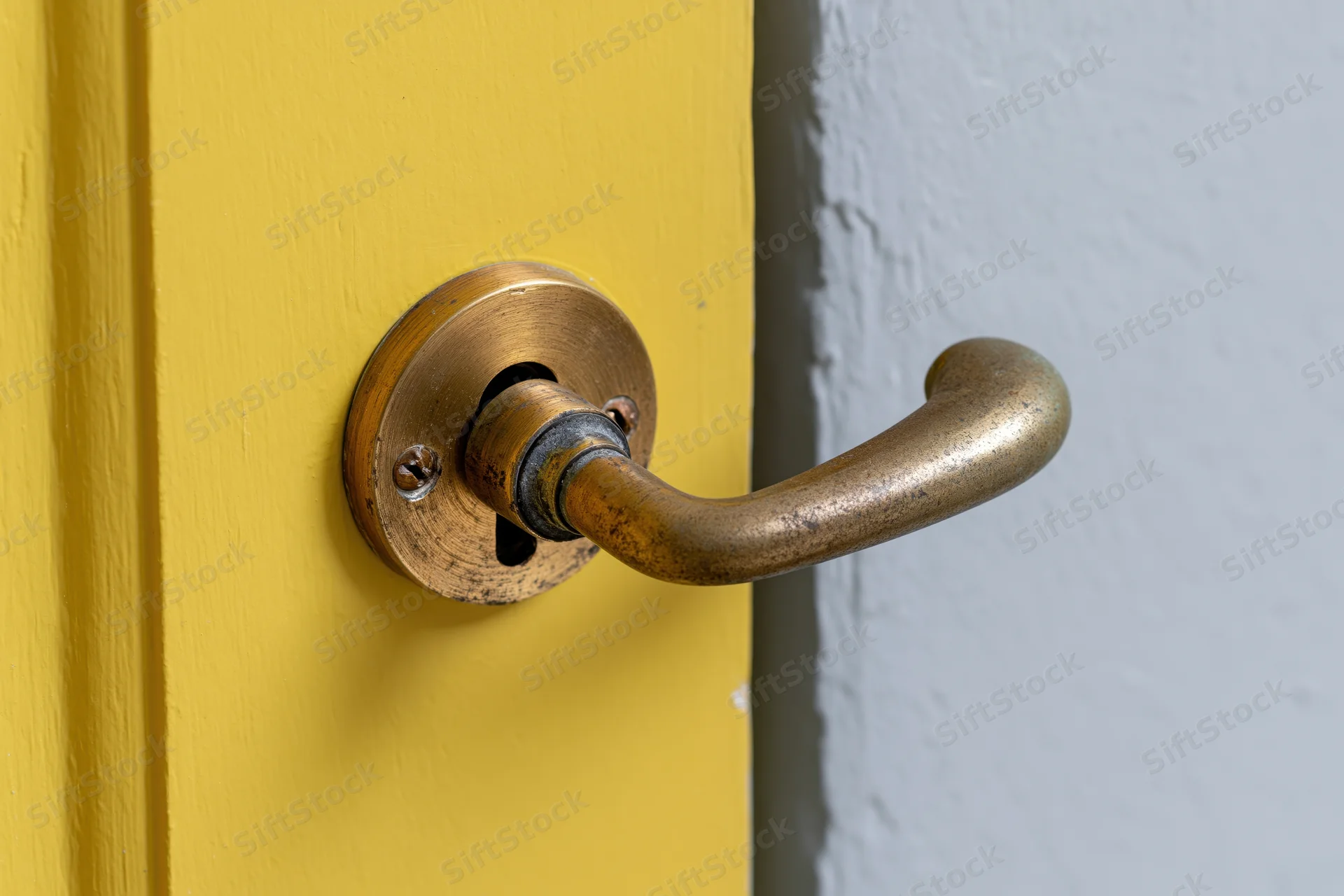 Aged brass door handle with keyhole escutcheon on a yellow door