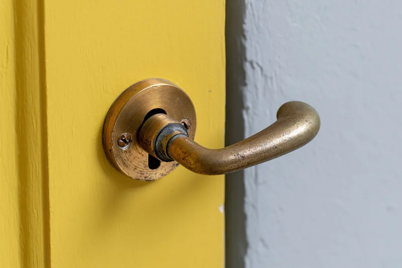 Aged brass door handle with keyhole escutcheon on a yellow door