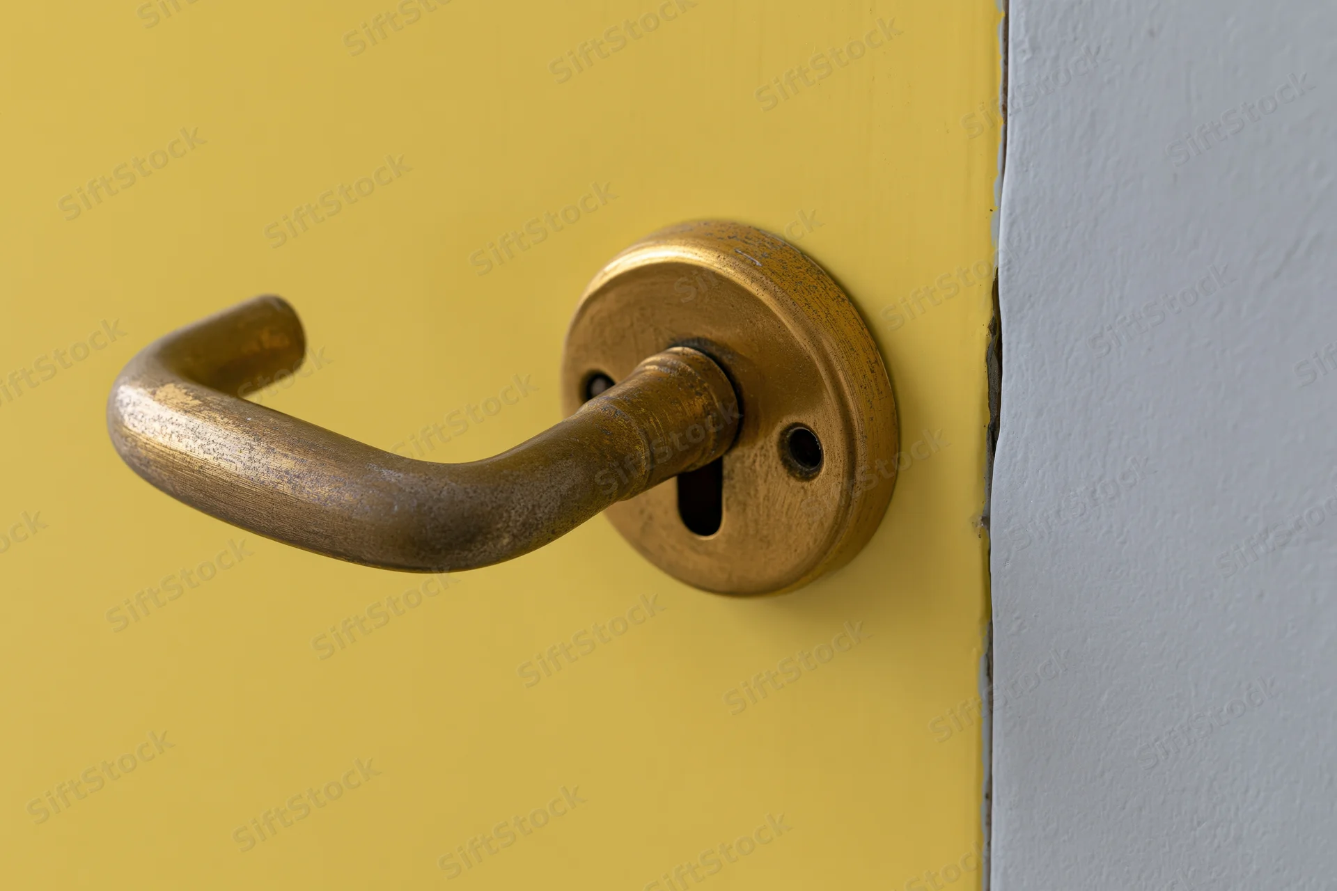 Aged brass door handle with keyhole escutcheon on a yellow door corner