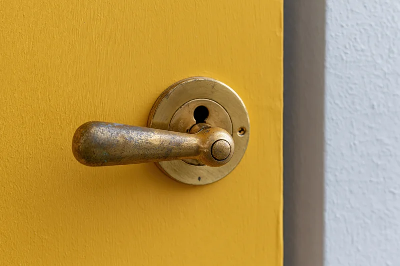 Aged brass door handle with keyhole escutcheon on a yellow door