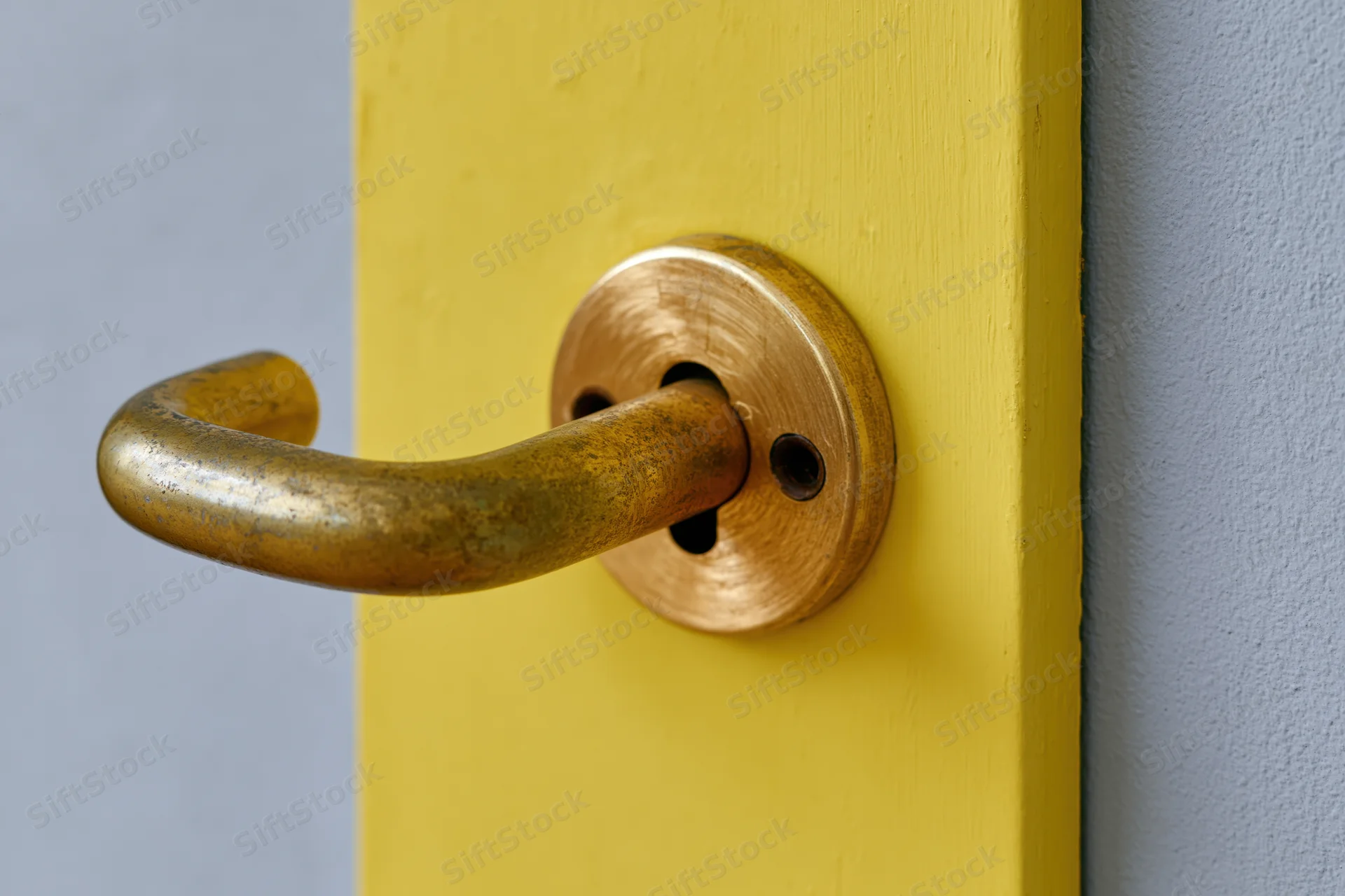 Aged brass door handle with keyhole escutcheon on a yellow door panel