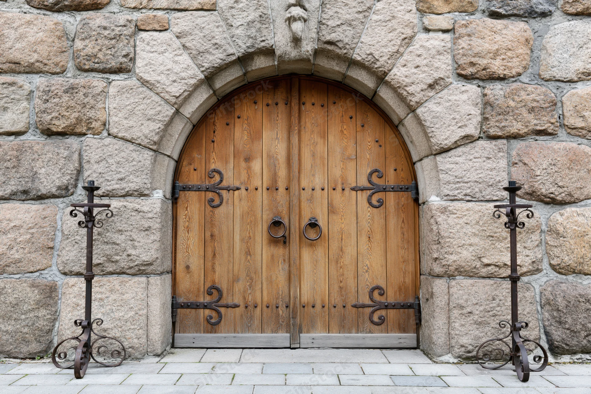Arched wooden double door with iron ring handles set in a stone wall