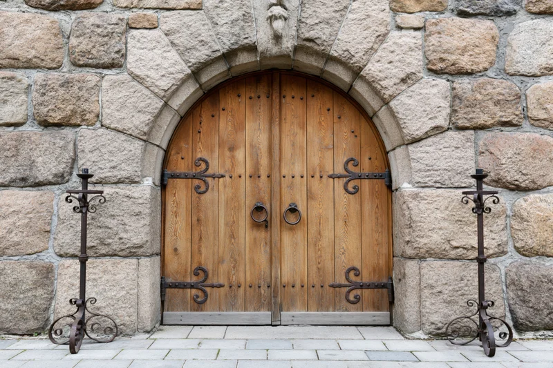 Arched wooden double door with iron ring handles set in a stone wall