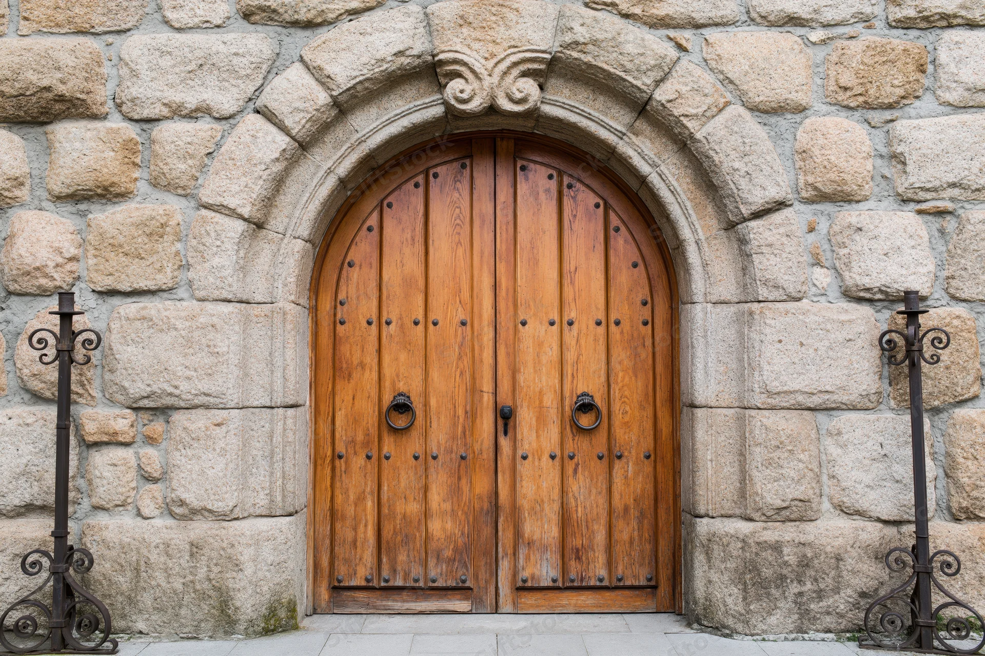 Arched wooden double door with iron ring handles set in a stone facade