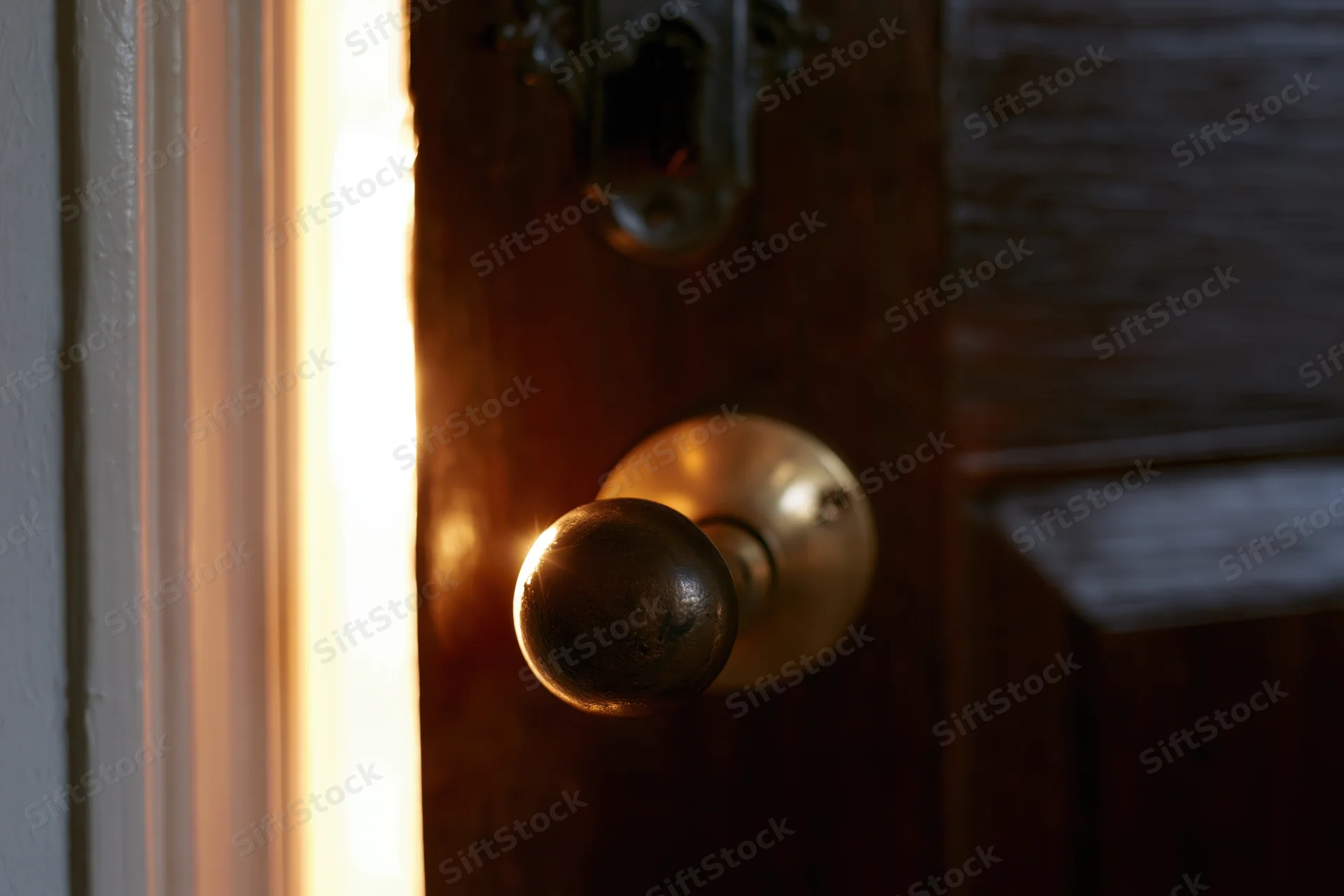 Old dark wooden door slightly ajar with worn brass knob and light glowing through the gap