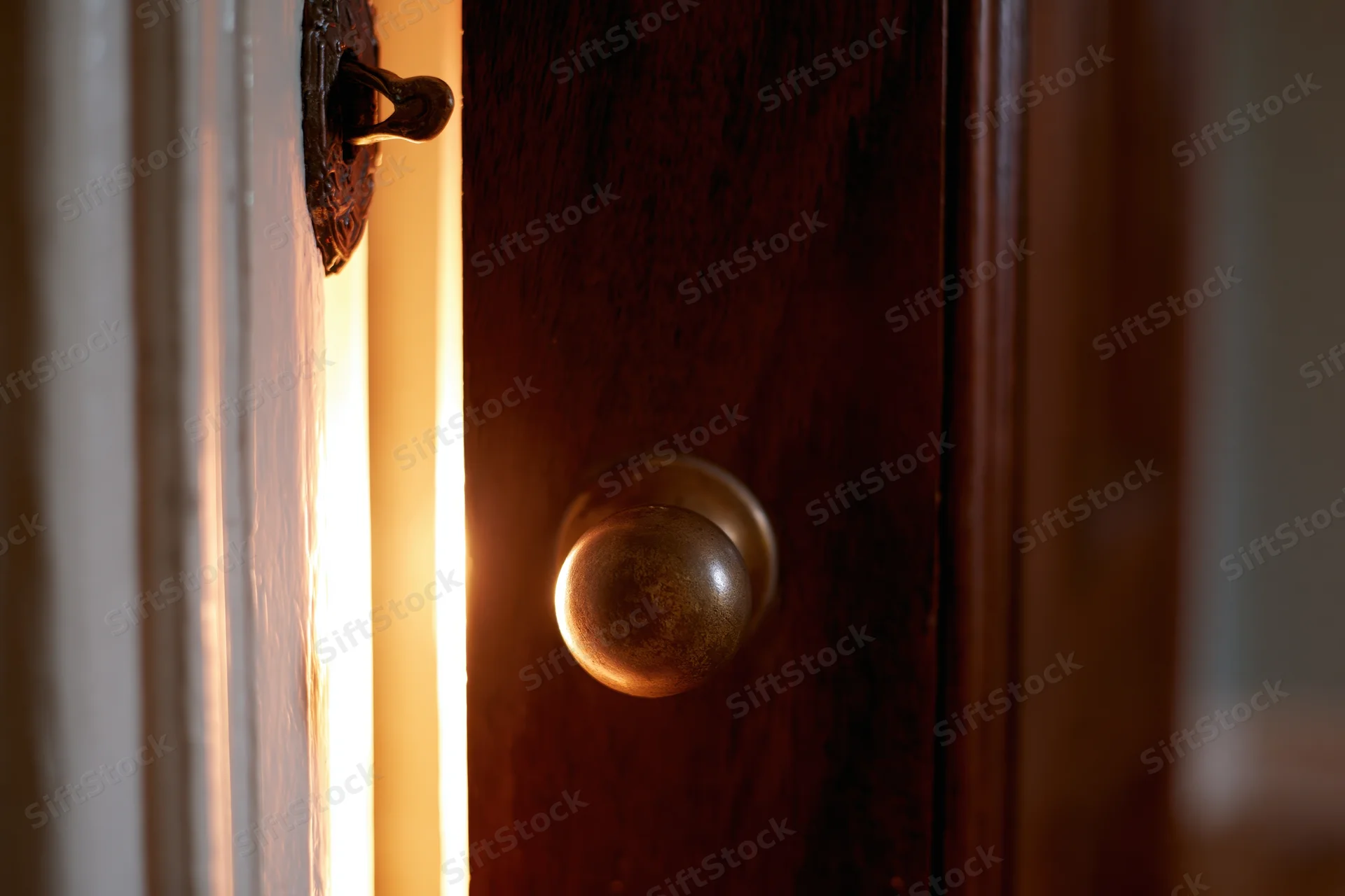 Old dark wooden door slightly ajar with brass knob and light glowing through the crack