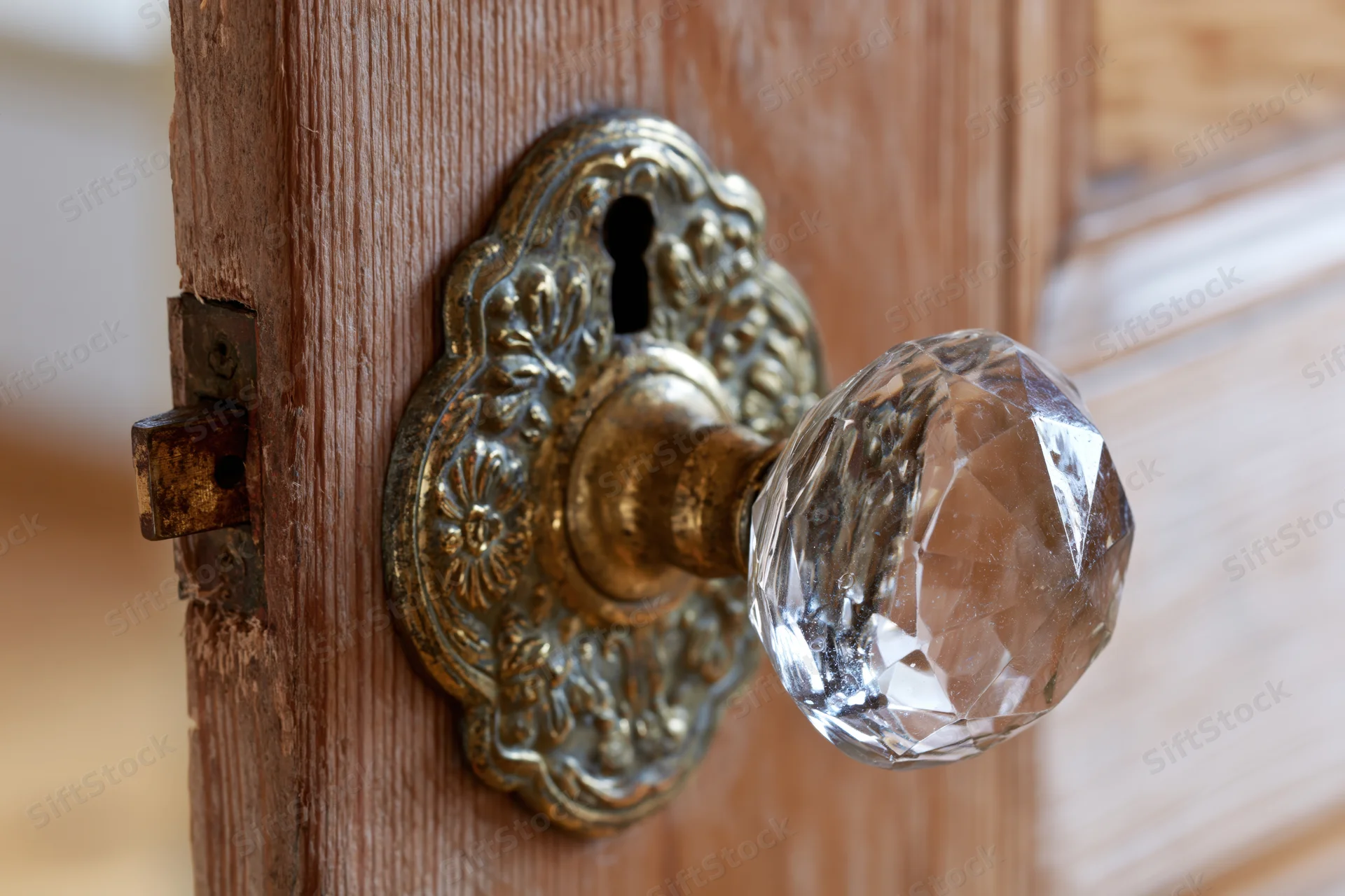 Antique faceted crystal glass door knob on ornate brass plate mounted on wooden door