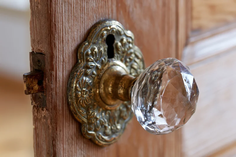 Antique faceted crystal glass door knob on ornate brass plate mounted on wooden door