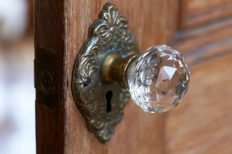 Closeup of an antique faceted crystal glass door knob on a wooden door with ornate brass plate and keyhole