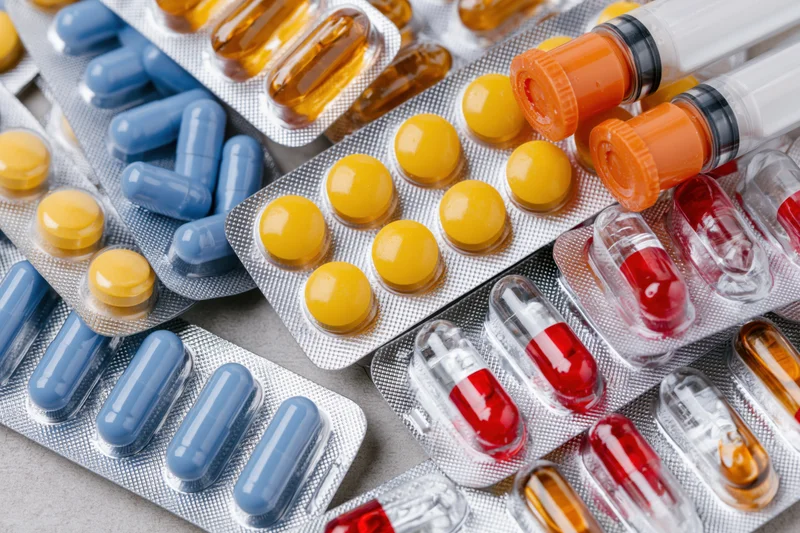 Assorted pharmaceutical blister packs with colorful pills and capsules arranged on a gray surface