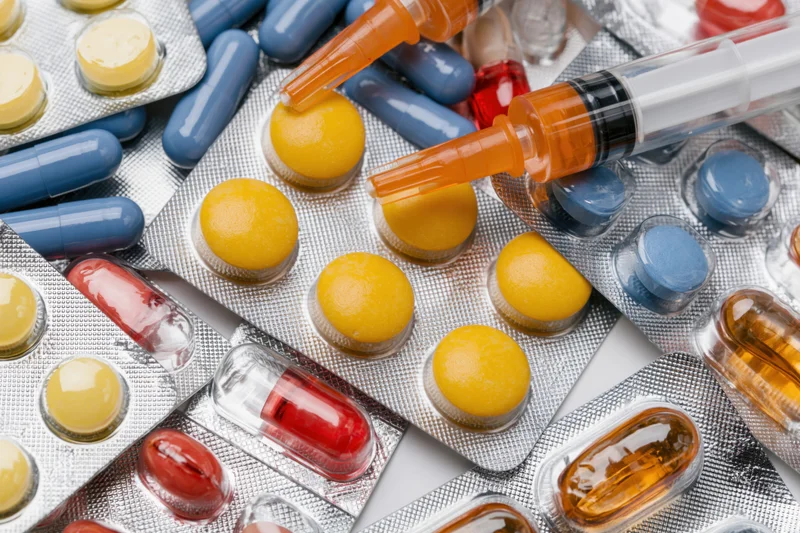 Assorted pharmaceutical blister packs with pills and capsules in various colors arranged in close-up flat lay