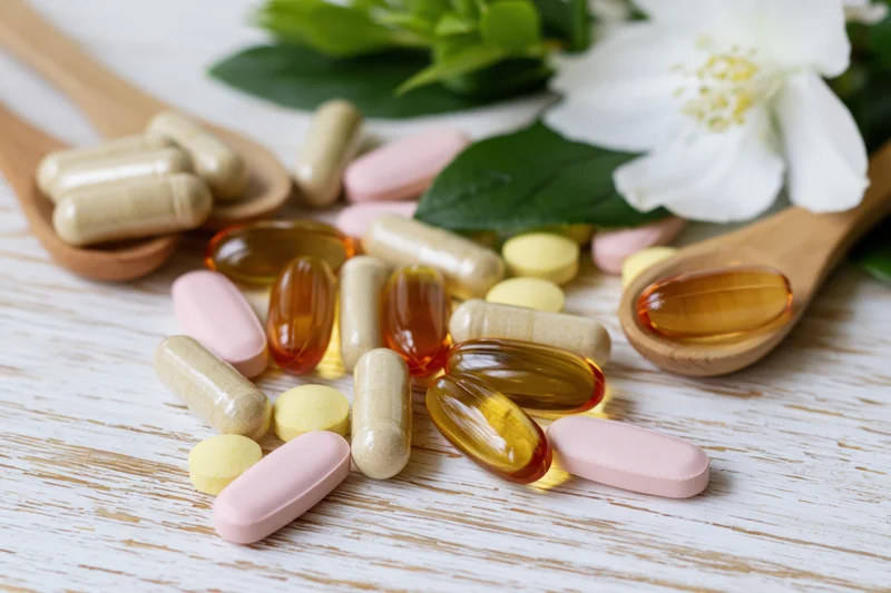 Assorted dietary supplements and vitamins in wooden spoons with flowers on a white wooden surface
