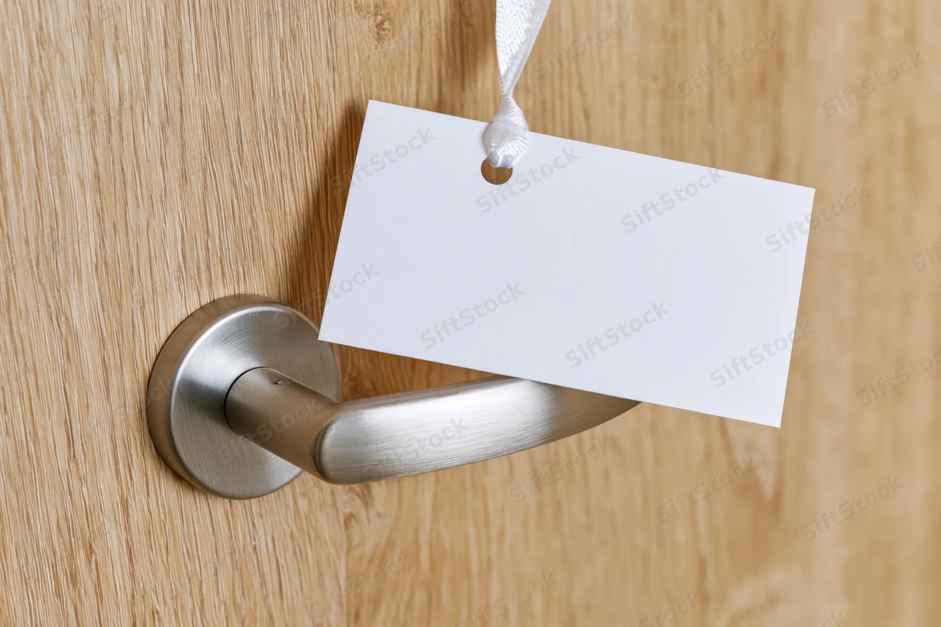 Blank white door hanger sign hanging from brushed steel door handle on wooden door