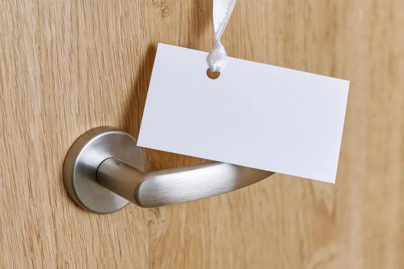 Blank white door hanger sign hanging from brushed steel door handle on wooden door