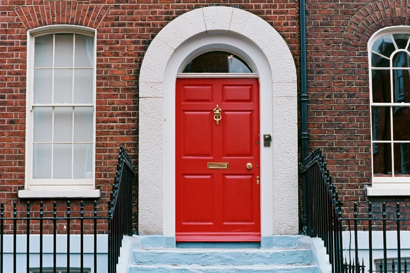 Bright red georgian front door with brass knocker and letterbox set in brick facade with stone arch and black iron railing