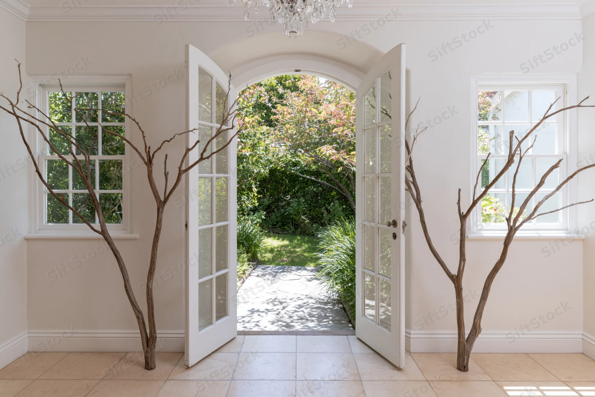 White arched doors open to a garden pathway from a cottage-style entryway