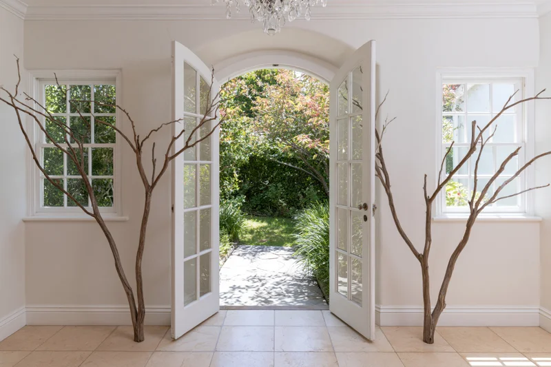 White arched doors open to a garden pathway from a cottage-style entryway