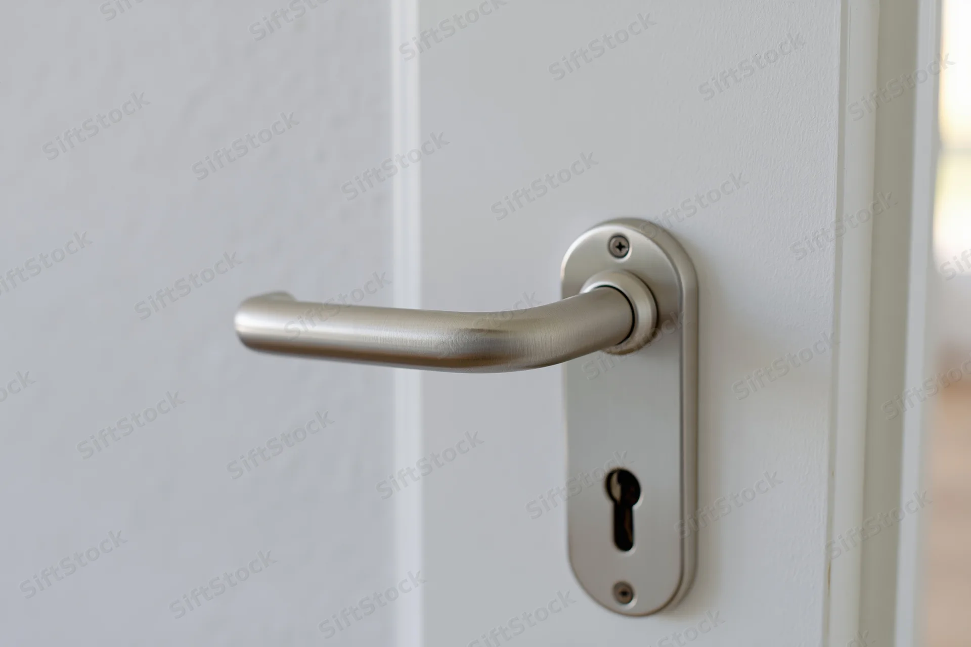 Brushed aluminum lever door handle with keyhole on white door closeup