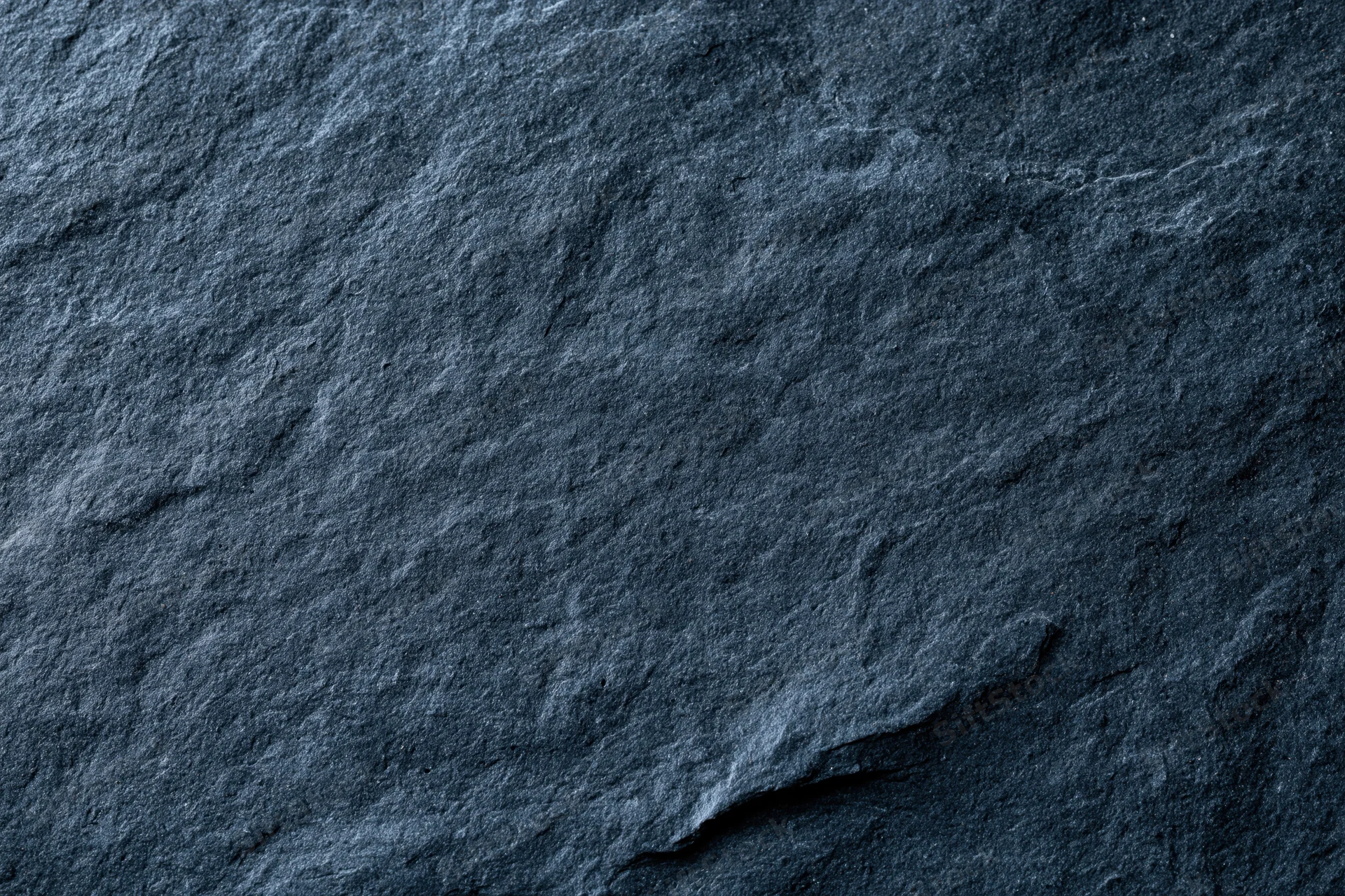 Close-up of dark slate stone surface with natural texture and cracks filling the frame