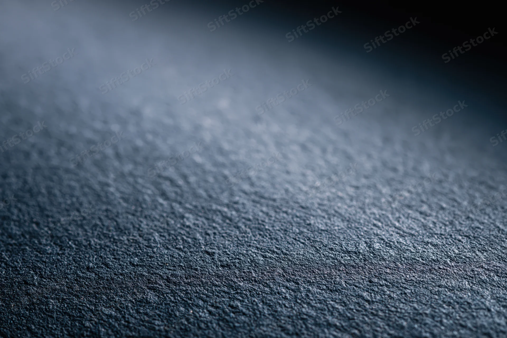 Close-up of a matte dark charcoal textured surface with fine grain and soft lighting gradient