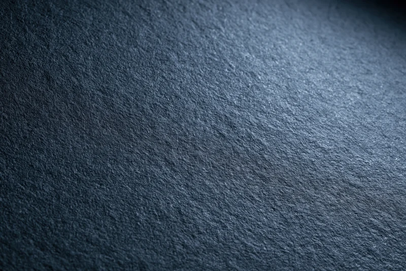 Close-up of a matte dark charcoal textured surface with fine grain and subtle lighting gradient