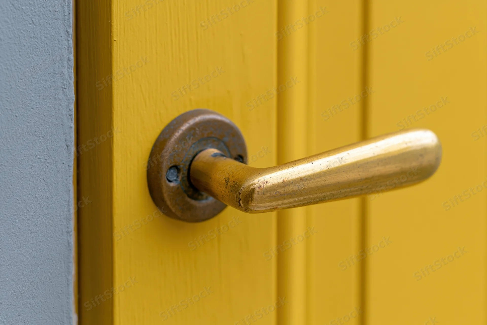 Brass lever door handle on a yellow wooden door with aged patina