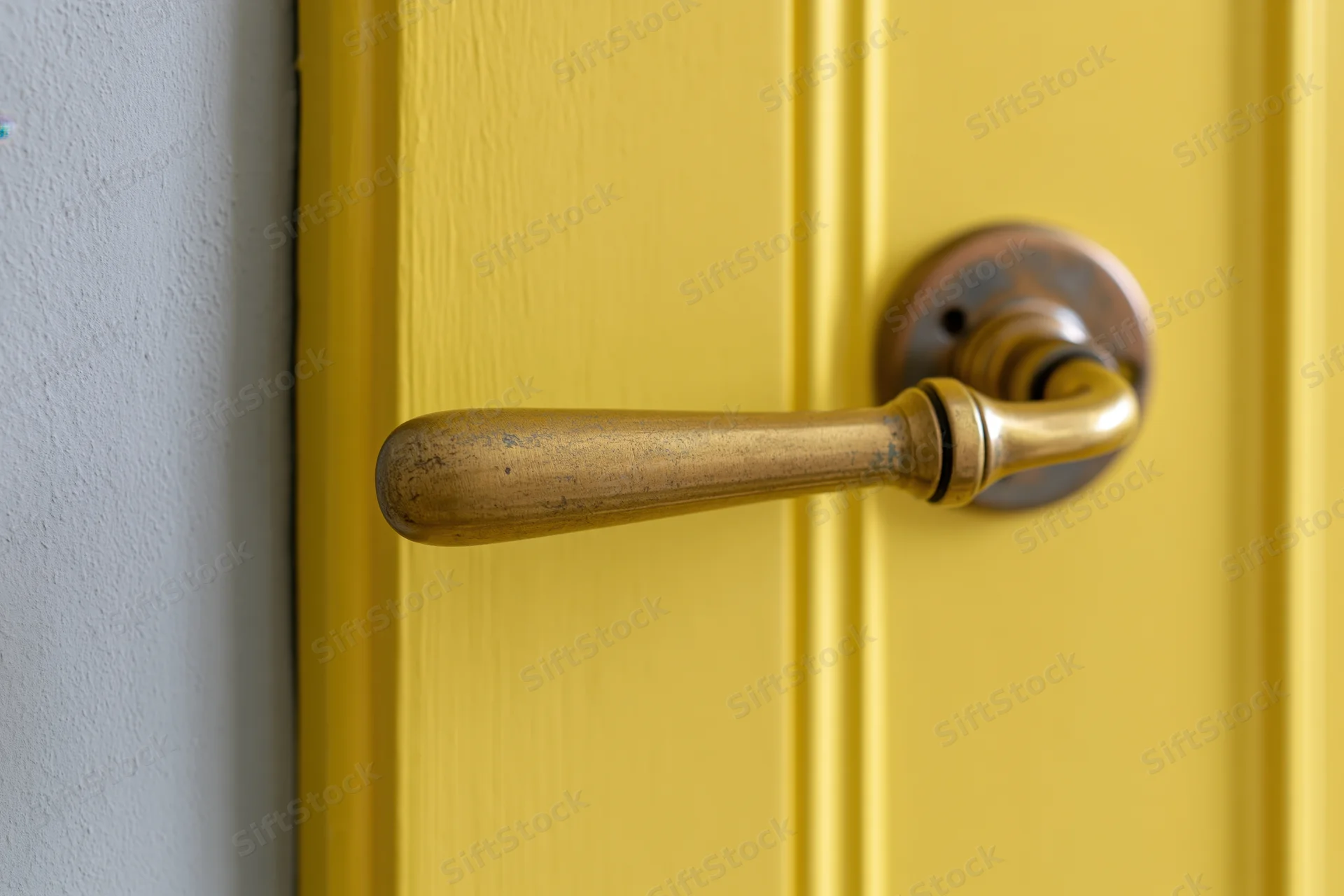 Brass lever door handle on a yellow wooden door in an interior hallway
