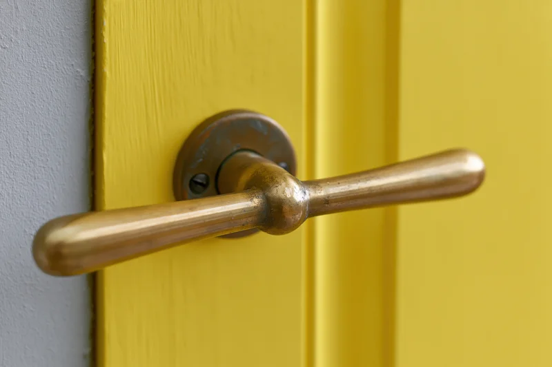 Brass lever door handle on a yellow wooden door