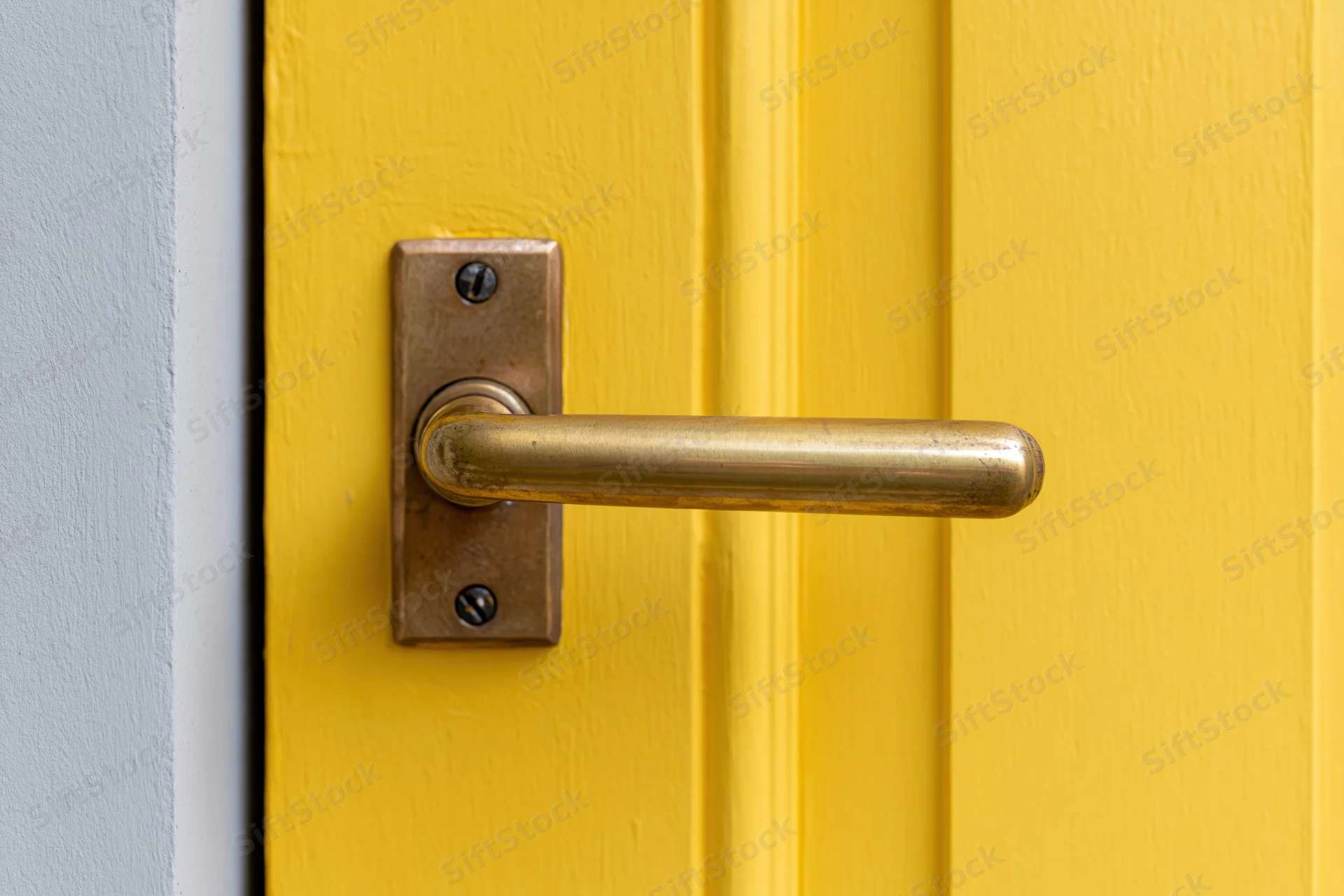 Brass lever door handle on a yellow painted door with gray frame