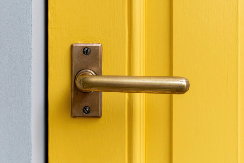 Brass lever door handle on a yellow painted door with gray frame