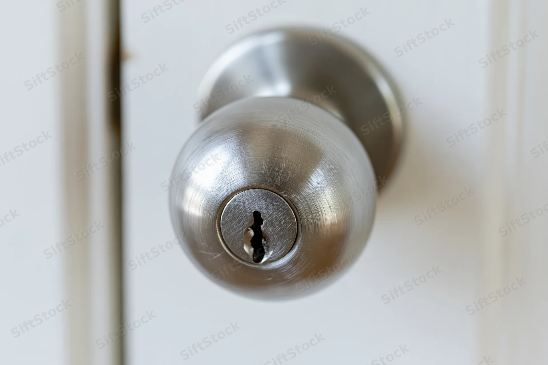 Close-up of a brushed stainless steel door knob with a keyhole on a white door