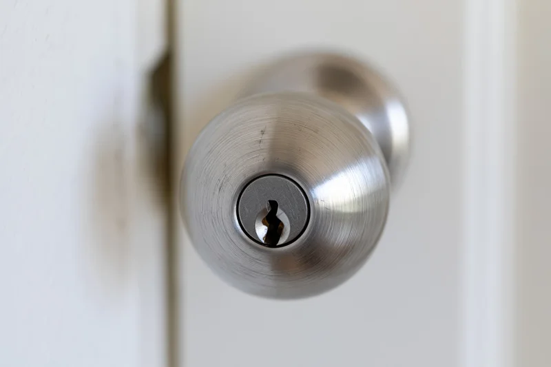 Close-up of a brushed stainless steel door knob with a keyhole on a white door