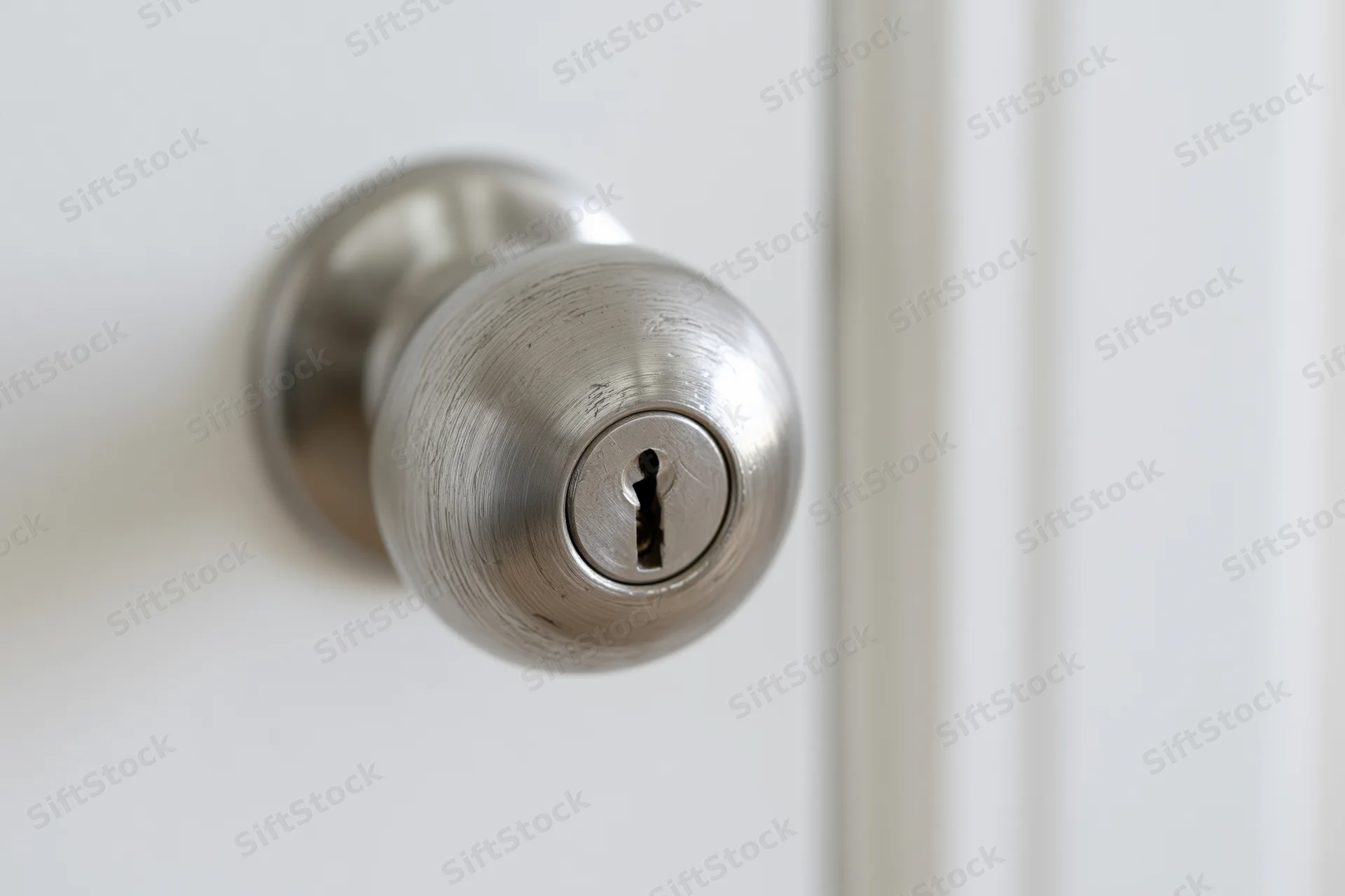 Close-up of a brushed stainless steel door knob with a keyhole on a white door
