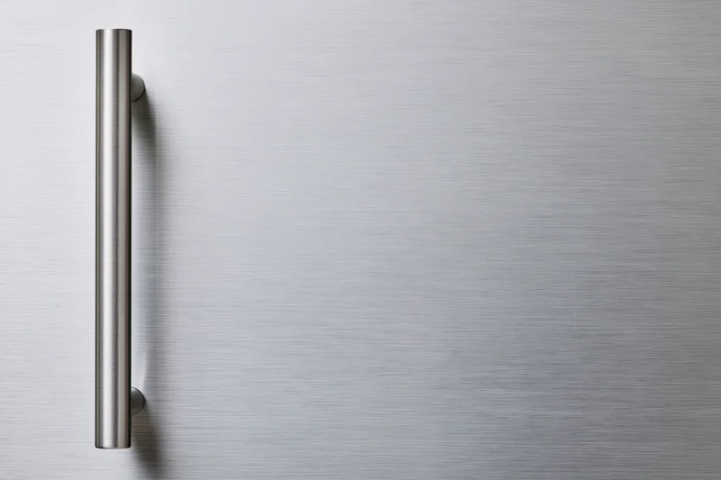 Brushed stainless steel refrigerator door with vertical handle on smooth surface