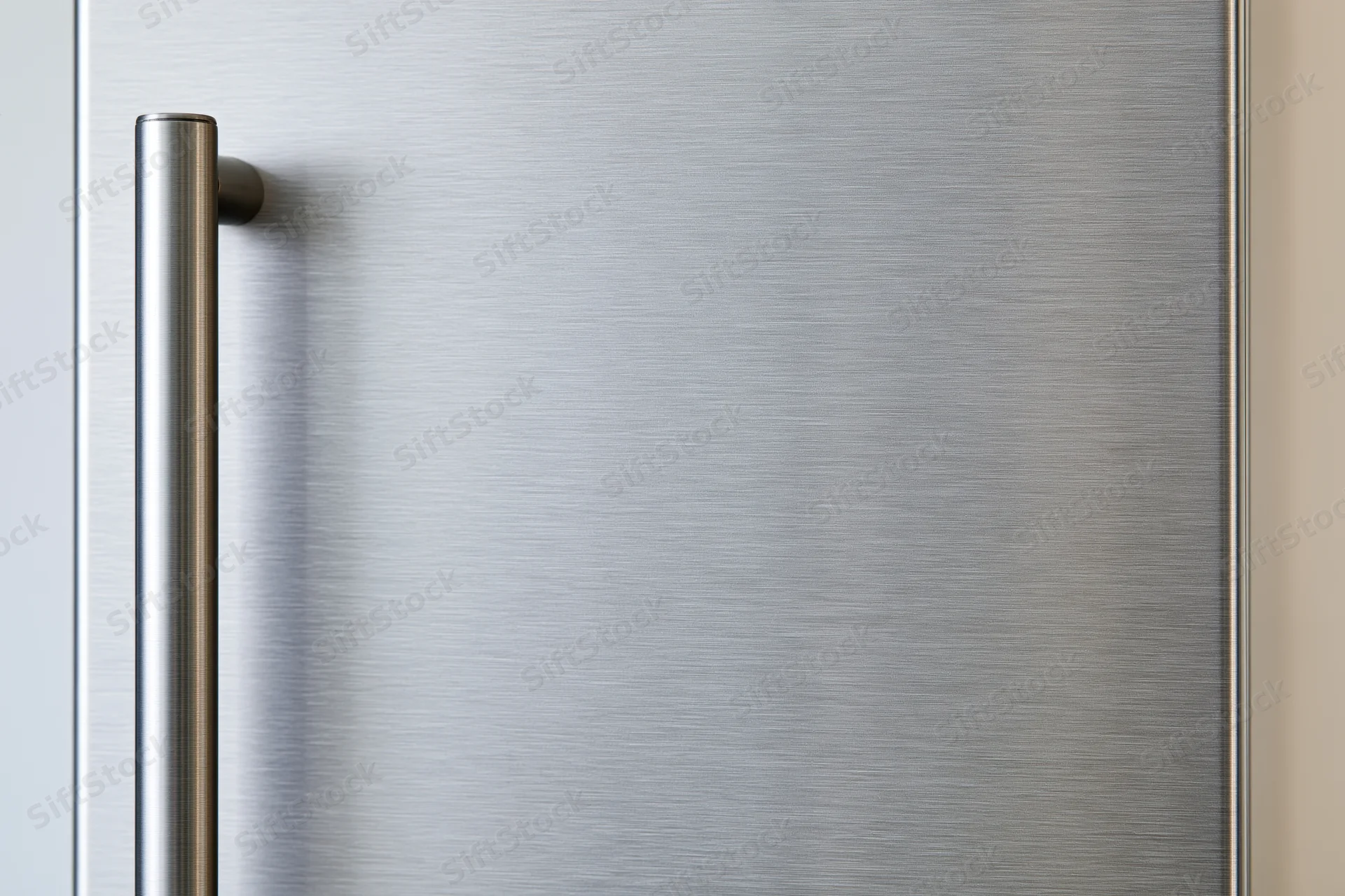 Close-up of a brushed stainless steel refrigerator door with vertical handle in a kitchen setting